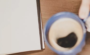 A person is holding a cup of coffee next to a notebook filled with top executive search solutions.