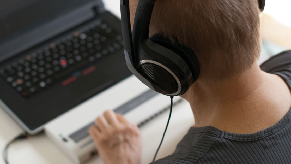 Person wearing headphones using a refreshable braille display in front of a laptop